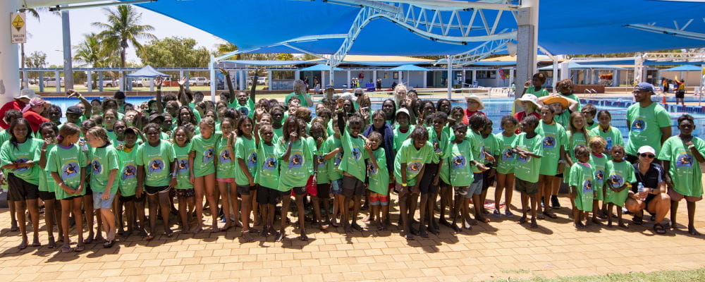 A group of aboriginal children with thier swim instructors and teachers, wearing green Spirit Carnival t-shirts by the pool at Port Hedland