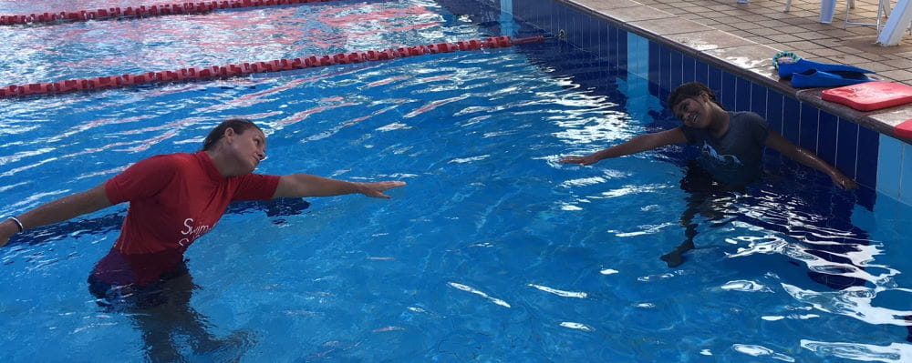 A swim instructor in the pool with an Aboriginal students practising swimming strokes