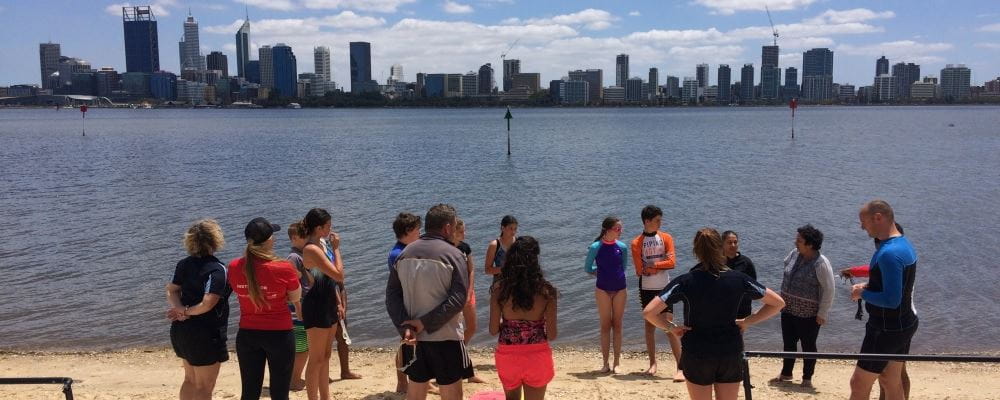 a group of children and adults gathered on the South Perth foreshore with the river and city in the distance