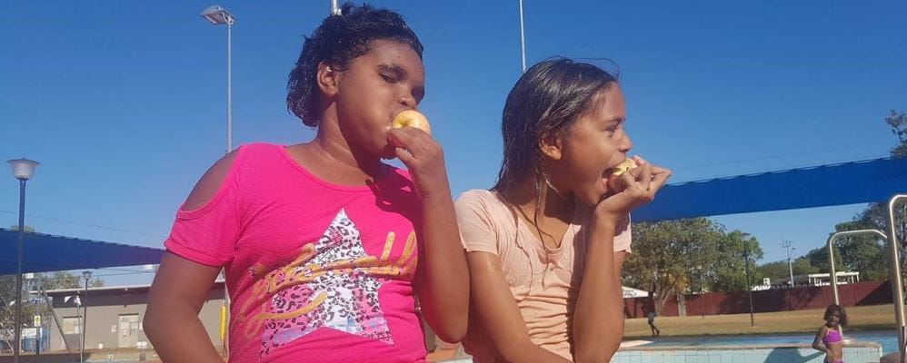 Two girls happily munch on apples as part of the Halls Creek Swim for Fruit program  