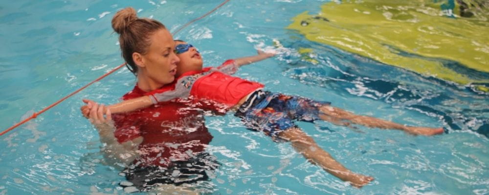 A swim instructor with a young boy floating on his back
