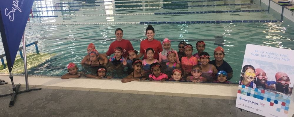 A group of multicultural girls in the water with two instructors smiling at the camera