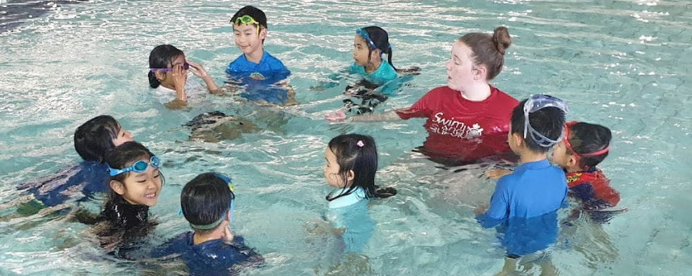 Multicultural children in the pool with their swim instructor