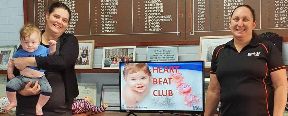 A heart beat club presentation with two women by a computer screen, one holding a baby