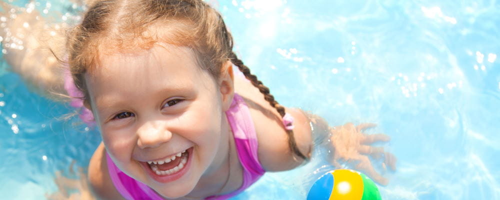 A toddler girl in a pool, smiling up at the camera