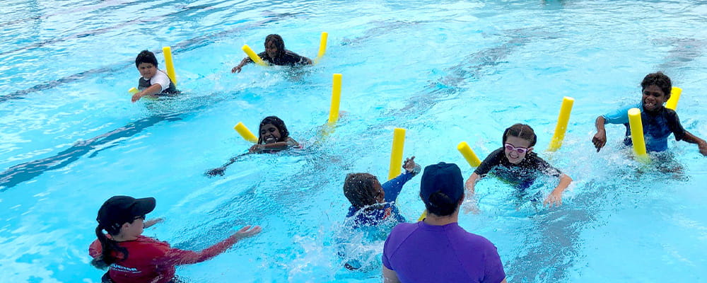 Children in the pool swimming on pool noodles