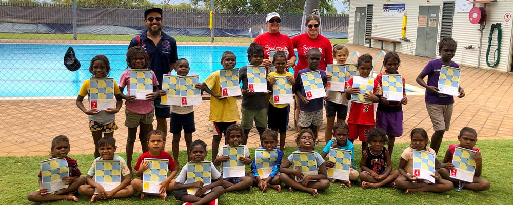 Children with their swimming certificates gathered by the pool with their instructors