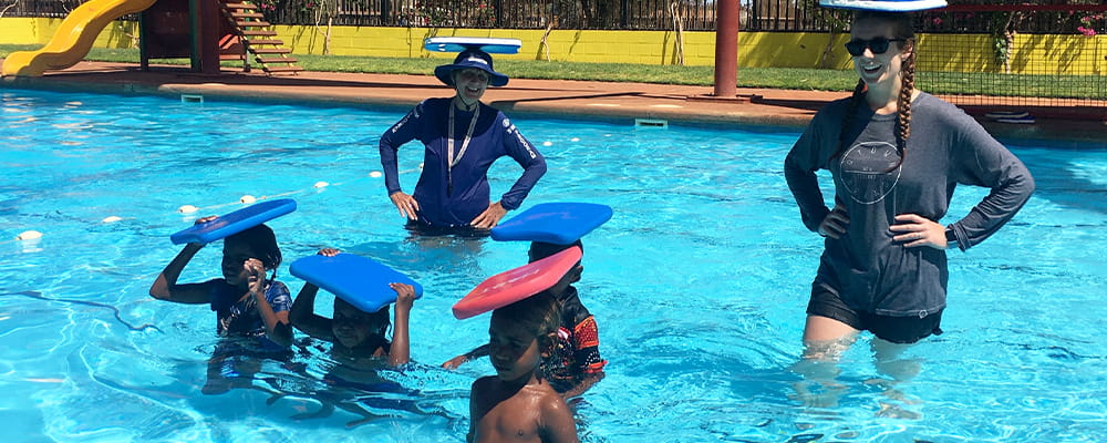Aboriginal children and their swimming instructors in a pool balancing kickboards on their heads