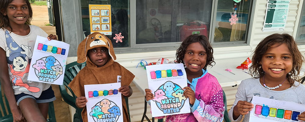Four Aboriginal children holding their Watch Around Water colouring sheets