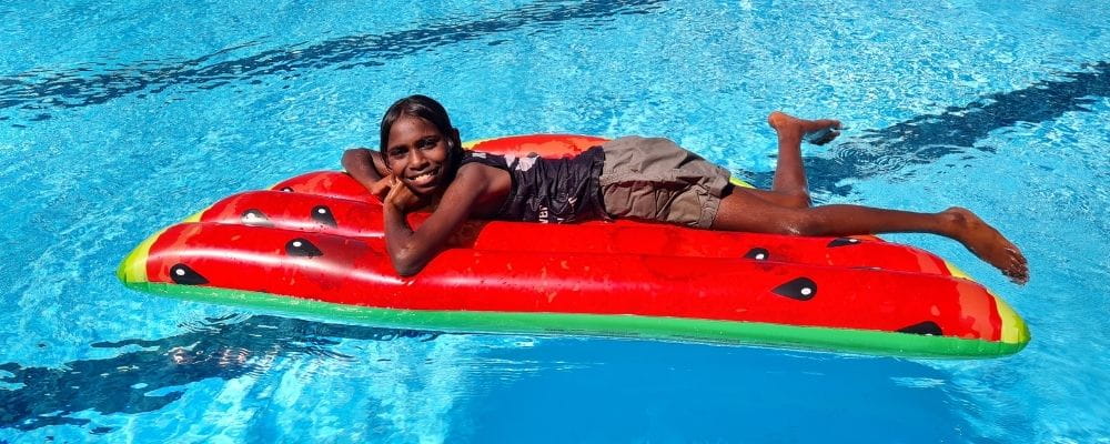 An Aboriginal girl laying in a watermelon inflatable in a pool