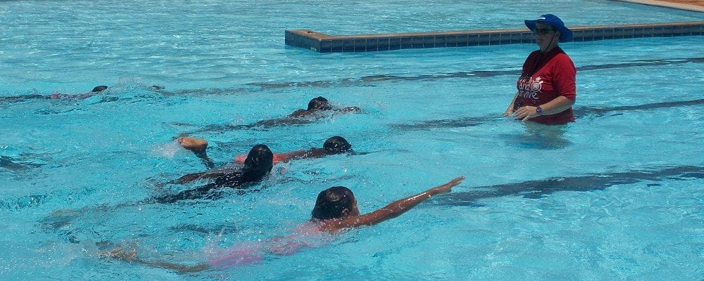 image of children swimming laps with instructor looking on