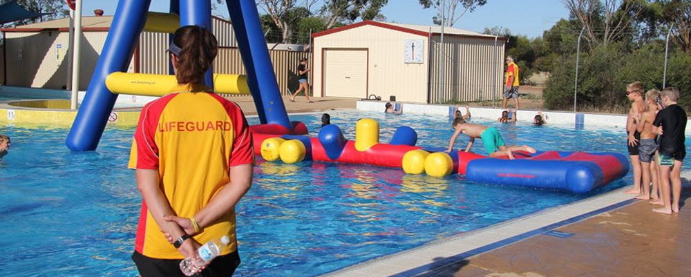 A lifeguard standing by the pool watching kids get on an inflatable