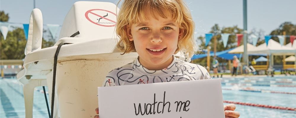 image of a child by a pool holding a sign saying "Watch Me"