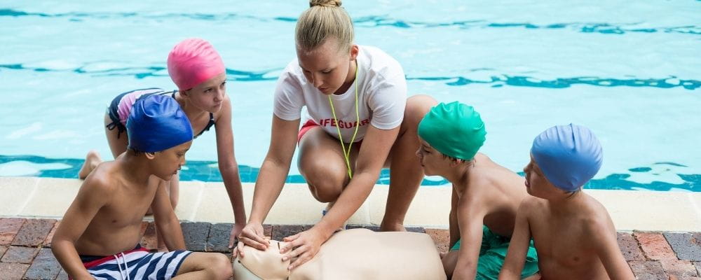 Children learning CPR with a lifeguard by a pool