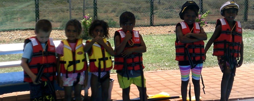 a group of 6 Aboriginal children wearing lifejackets and standing on the edge of a pool
