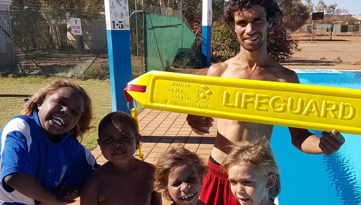 four young Aboriginal boys standing next to Pool Attendant at Burringurrah community pool
