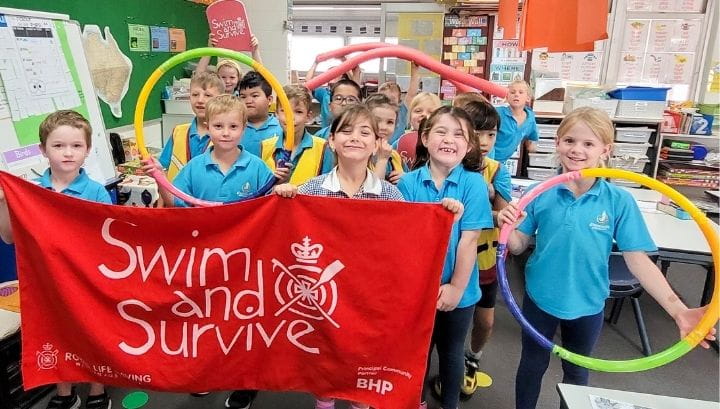 Students in a classroom standing with a Swim and Survive banner