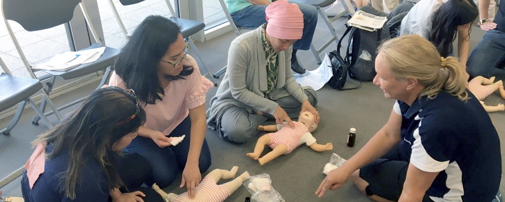 Three women practising CPR on a baby mannequin, with a Royal Life Saving trainer teaching them