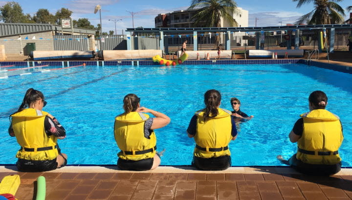 Four trainees sitting on the edge of the pool with lifejackets on