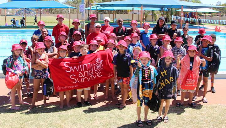 Children at our Goldfields Swimming and Lifesaving Carnival standing by Leiinster Pool with red Swim and Survive merchandise