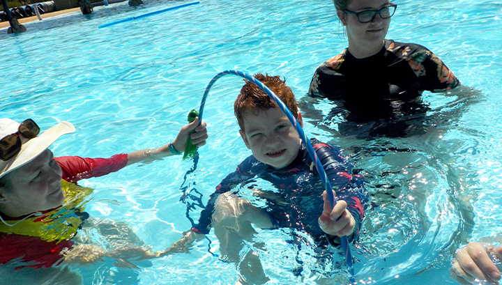 A swim instructor in the pool with a student going through a hoop