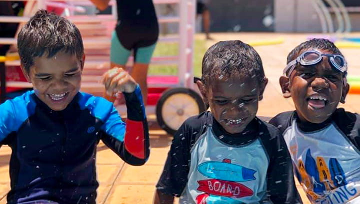 Three Aboriginal children laughing on the side of the pool
