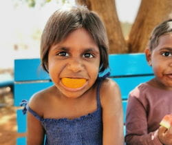 An Aboriginal girl with an orange in her mouth