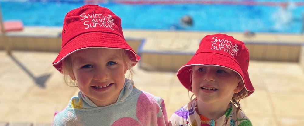 two little girls at a swim school open day wearing swim and survive bucket hats
