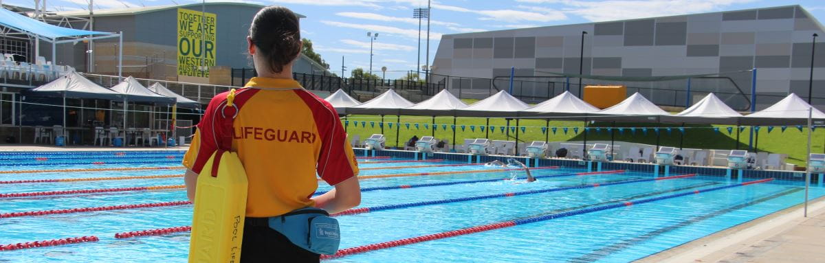 A lifeguard standing by a pool with a rescue tube