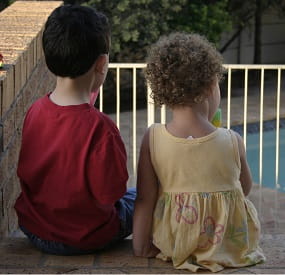 Kids sitting by pool looking at pool fence