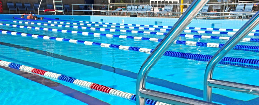 Picture of a public swimming pool with lane ropes, an access ladder and patrons in the background.