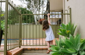 A young girl reaching up to open a pool fence