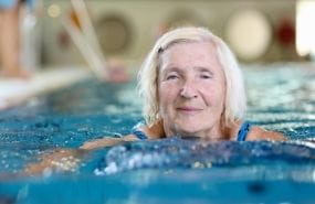 Elderly woman in pool swimming towards camera