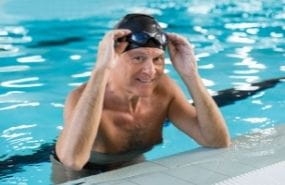 Middle aged man in swim cap and goggles at edge of pool