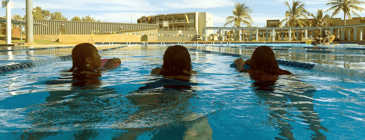 three aboriginal girls swimming away from camera in swimming pool