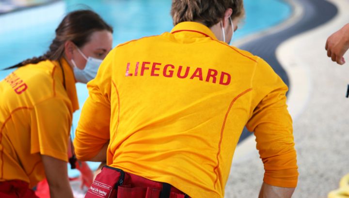 Three lifeguards leaning over practice manikin next to the pool