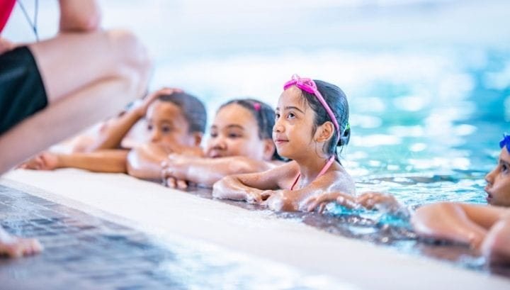 Children on edge of pool listening to teacher