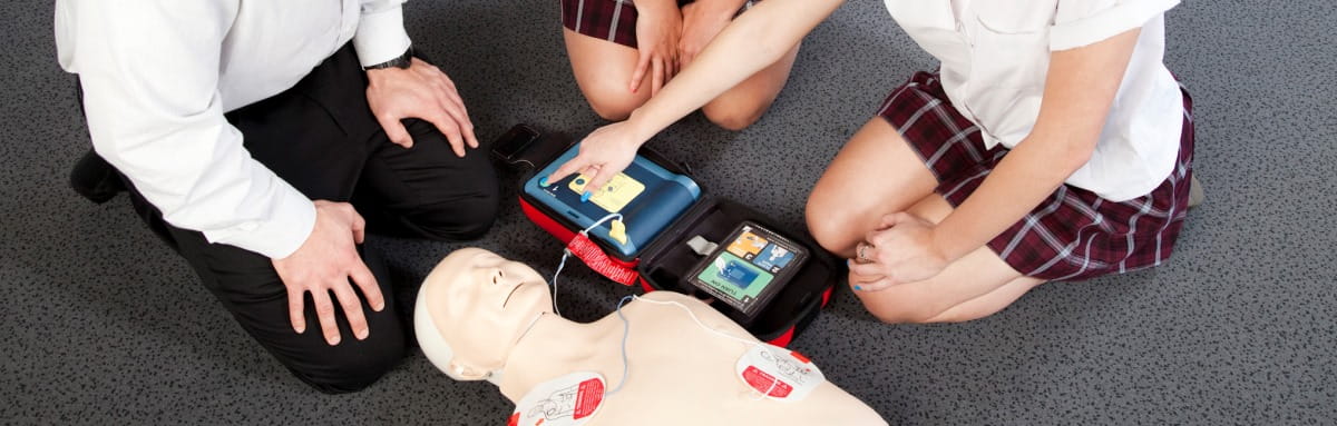 image of people gather around a CPR manikin attaching a defib