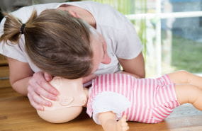A woman practising CPR on a baby manikin