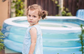 A toddler girl standing near a portable pool