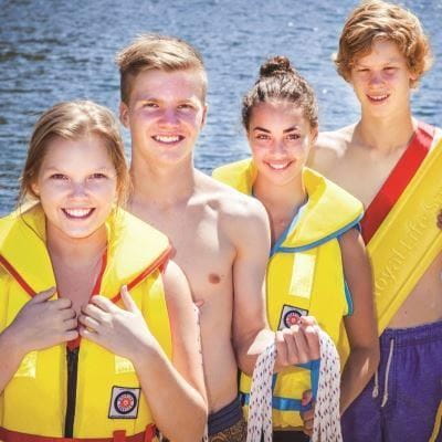 Four young people wearing yellow lifekackets and holding ropes and flotation devices