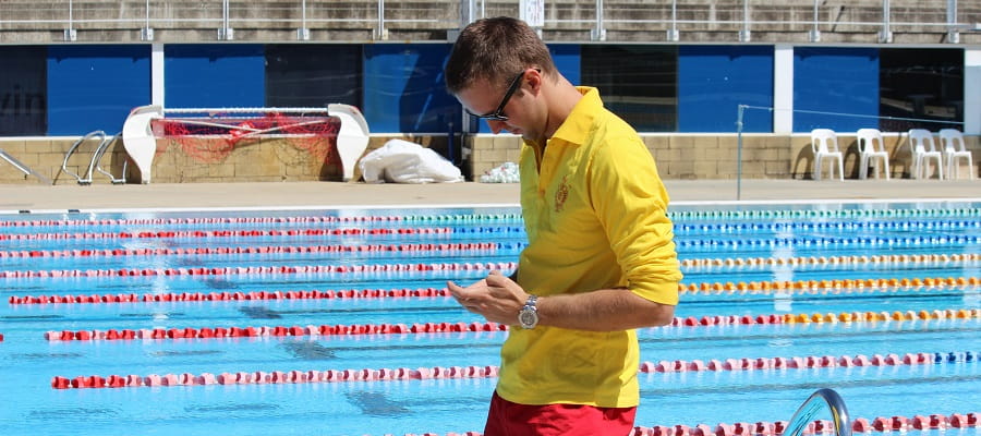 male pool lifeguard looking down at mobile phone and not paying attention to the pool
