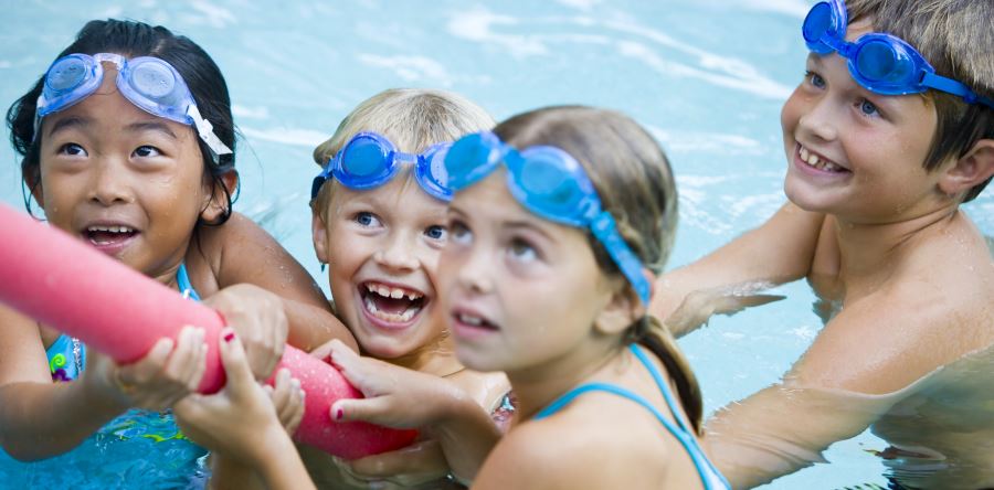 Four children wearing blue goggles and holding a pool noodle