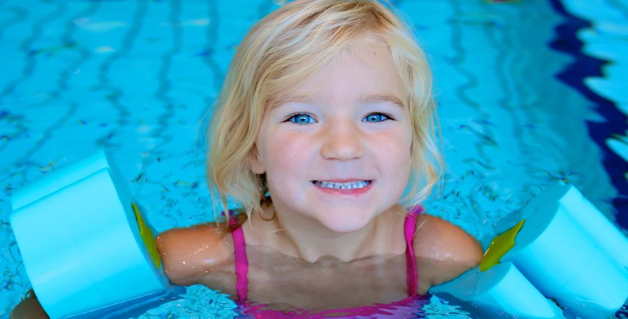 A pre school aged girl wearing blue floaties and holding onto the pool edge