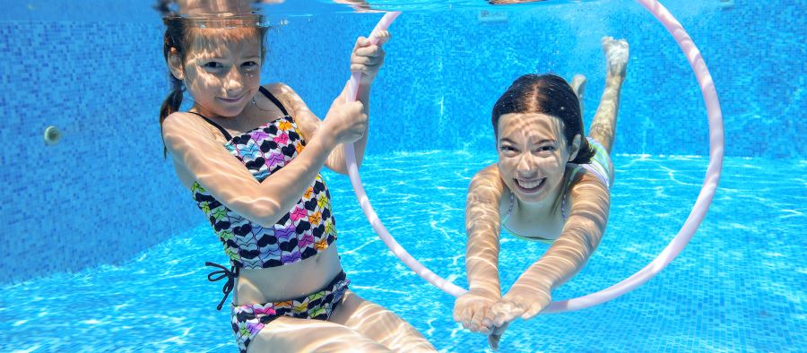 two girls playing with a hula hoop underwater in a pool