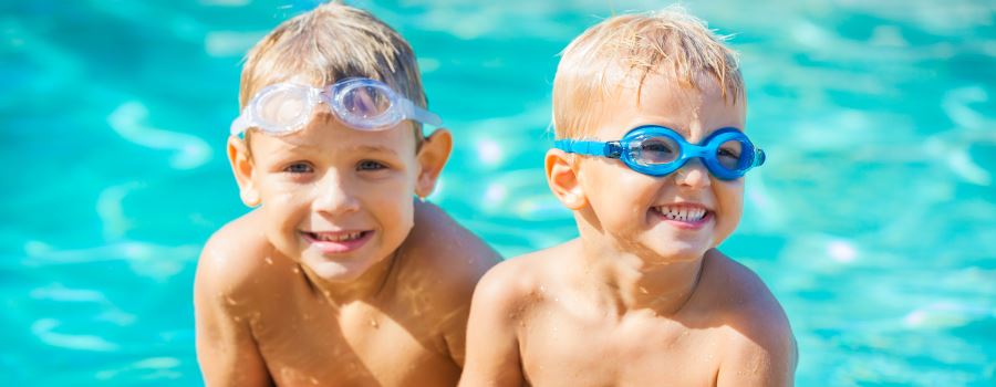 Two blond-haird little boys in a pool wearing goggles