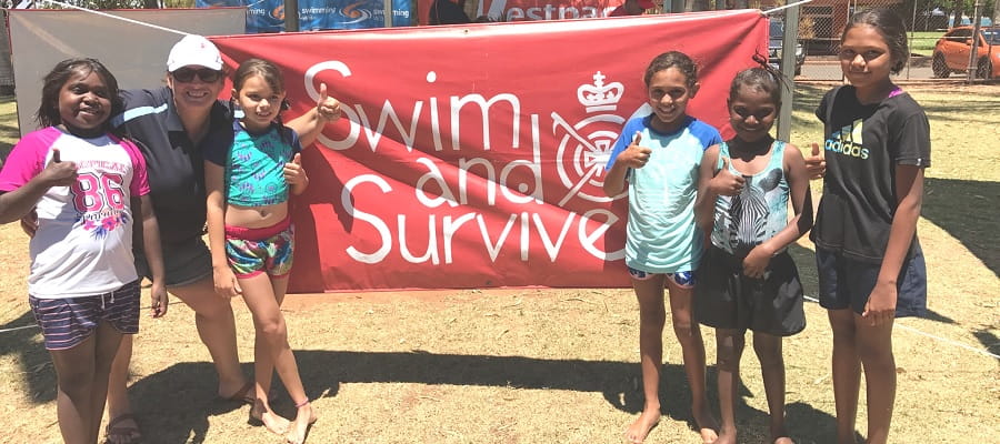young Aboriginal girls standing in front of a Swim and Survive banner