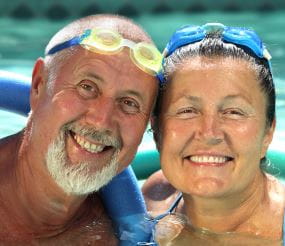An elderly man and woman with goggles on their head in a pool