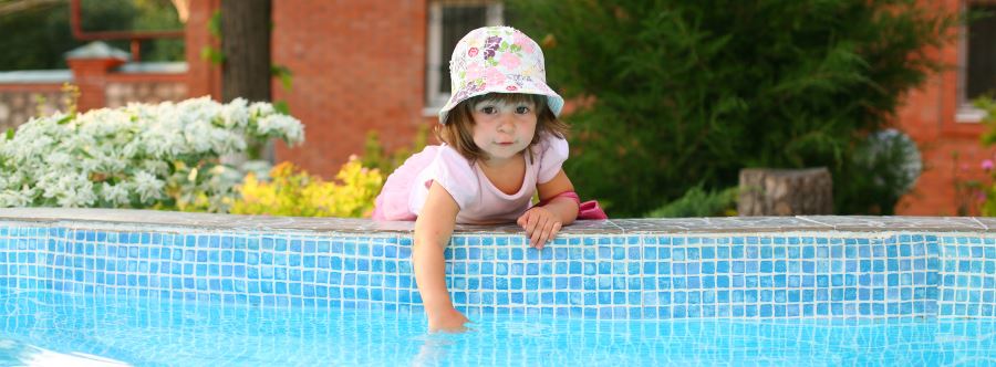 A toddler girl leaning over the edge of a pool putting her hand in the water