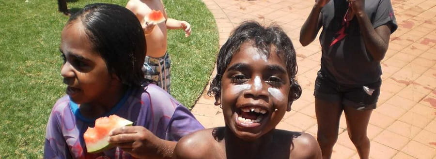 An aboriginal girl and boy smiling at the camera with watermelon in their hands